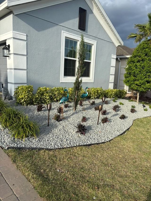 Curved bed with white rock, red-leaf plants and garden lights along the side of a gray house